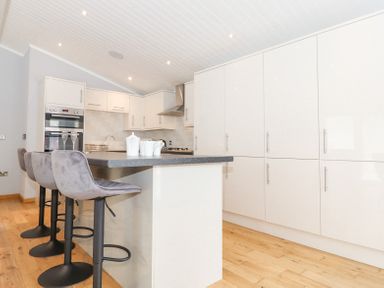 A kitchen with bar stools at a countertop ovens and cabinets along a wall at Lakes Lodge Keswick Court 3 White Cross Bay near Windermere