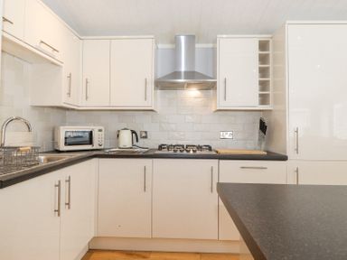 A kitchen with white cabinets black countertops a gas stove microwave kettle and a knife block at Lakes Lodge Keswick Court 3 White Cross Bay near Windermere