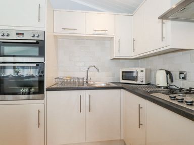 A kitchen with white cabinets a sink a microwave a kettle a gas stove and an oven at Lakes Lodge Keswick Court 3 White Cross Bay near Windermere