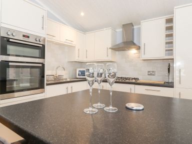 A kitchen with three wine glasses on a table ovens sink and stove at Lakes Lodge Keswick Court 3 White Cross Bay near Windermere