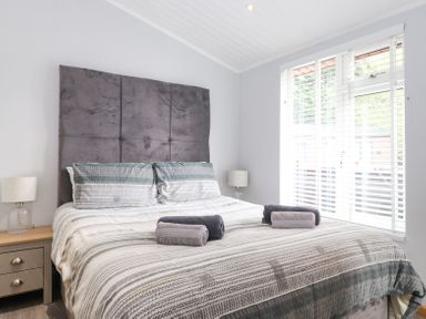 A bedroom with a bed with folded towels on it bedside tables with lamps and a window with blinds at Lakes Lodge Keswick Court 3 White Cross Bay near Windermere