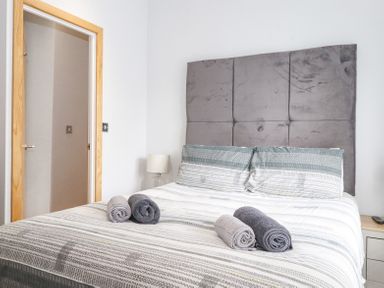 A bedroom with a double bed rolled towels bedside table with lamp and an open door at Lakes Lodge Keswick Court 3 White Cross Bay near Windermere