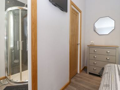 A bedroom corner with a grey chest of drawers and mirror a wooden door and a shower area at Lakes Lodge Keswick Court 3 White Cross Bay near Windermere