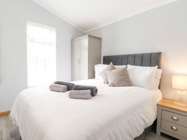A bedroom with a bed with white bedding and folded towels on it next to a nightstand with a lamp and a wardrobe at Lakes Lodge Keswick Court 3 White Cross Bay near Windermere