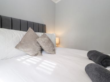 A bed with white sheets two gray pillows and two rolled dark towels at Lakes Lodge Keswick Court 3 White Cross Bay near Windermere