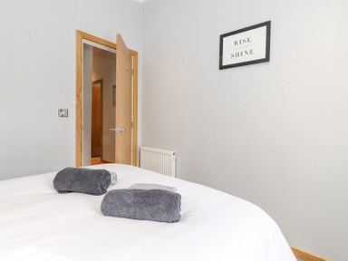 A bedroom with a bed with folded towels a partially open wooden door and a framed rise and shine sign on the wall at Lakes Lodge Keswick Court 3 White Cross Bay near Windermere