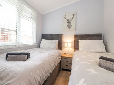 A bedroom with two single beds with towels on them a bedside table with a lamp and a deer wall art at Lakes Lodge Keswick Court 3 White Cross Bay near Windermere