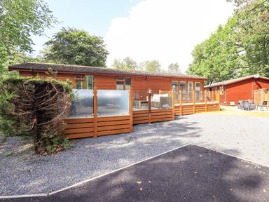 A wooden lodge with a fenced patio area and outdoor furniture surrounded by trees at Lakes Lodge Keswick Court 3 White Cross Bay near Windermere