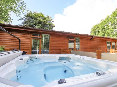 An outdoor hot tub filled with water in front of a wooden cabin with windows at Lakes Lodge Keswick Court 3 White Cross Bay near Windermere