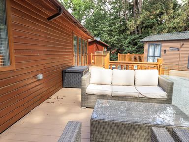 An outdoor patio with a wicker sofa with cushions and a glass coffee table at Lakes Lodge Keswick Court 3 White Cross Bay near Windermere