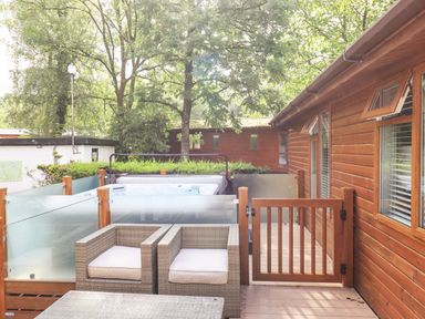 An outdoor wooden deck with two wicker chairs and a hot tub surrounded by frosted glass panels at Lakes Lodge Keswick Court 3 White Cross Bay near Windermere