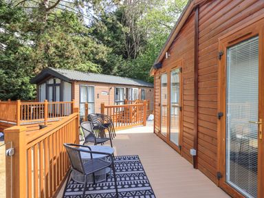 An outdoor deck area with black chairs and a table next to a wooden building with glass doors at Lakes Lodge in Keswick Court 3 White Cross Bay near Windermere