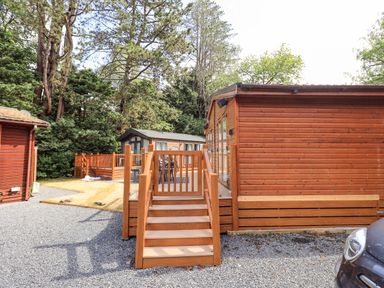 A wooden cabin with stairs and deck surrounded by trees and gravel driveway at Lakes Lodge Keswick Court 3 White Cross Bay near Windermere