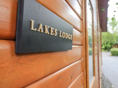 A black sign with lakes lodge written on a wooden wall outside a building at Lakes Lodge Keswick Court 3 White Cross Bay near Windermere