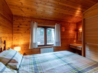 A bedroom with wooden walls a bed bedside table a lamp and a window at Glaramara Number 7 Burnside Park near Keswick