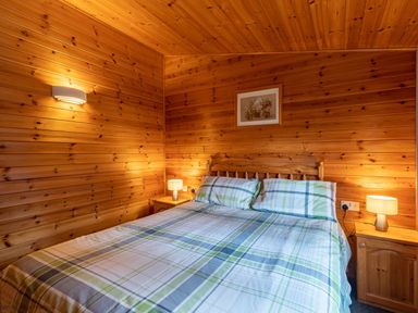 A bedroom with a double bed with checked bedding two bedside tables with lamps and wooden panel walls at Glaramara Number 7 Burnside Park near Keswick