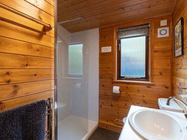 A bathroom with wooden walls a shower area a sink a window and a towel on a rack at Glaramara Number 7 Burnside Park near Keswick