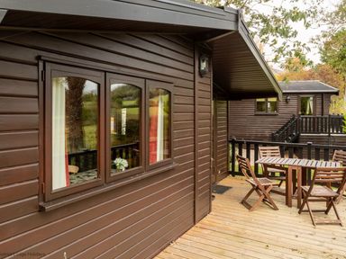 An outdoor wooden deck with a table and four chairs next to a brown wooden cabin at Glaramara Number 7 Burnside Park near Keswick