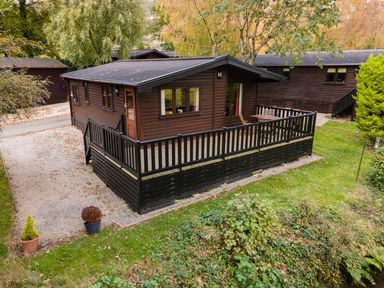 A wooden cabin with a fenced porch and outdoor furniture surrounded by trees and grass at Glaramara Number 7 Burnside Park near Keswick