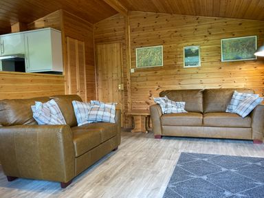 A living room with two brown leather sofas and plaid pillows wooden walls and framed maps at Glaramara Number 7 Burnside Park near Keswick