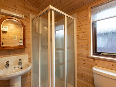 A bathroom with a shower cubicle a sink with taps a mirror and a window at Rivendell Burnside Park Number 14 Burnside Park near Keswick