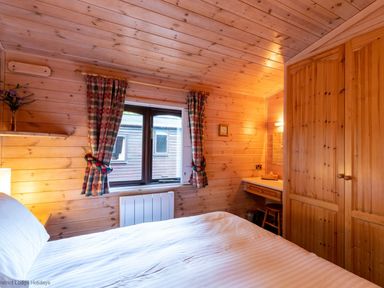 A bedroom with a wood paneled ceiling and walls a bed a window with plaid curtains and a wooden wardrobe at Rivendell Burnside Park Number 14 Burnside Park near Keswick