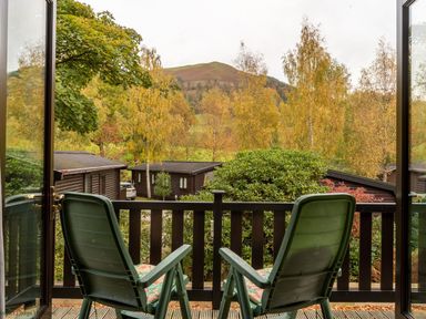 A balcony with two green chairs overlooking trees and cabins at Rivendell Burnside Park Number 14 Burnside Park near Keswick