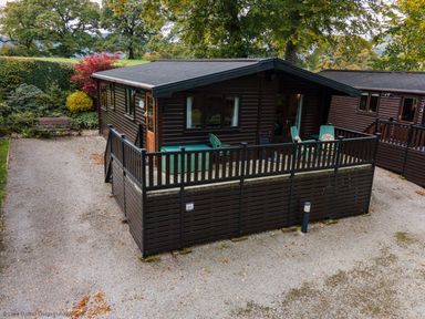 A small wooden cabin with a fenced porch and green chairs at Rivendell Burnside Park Number 14 Burnside Park near Keswick