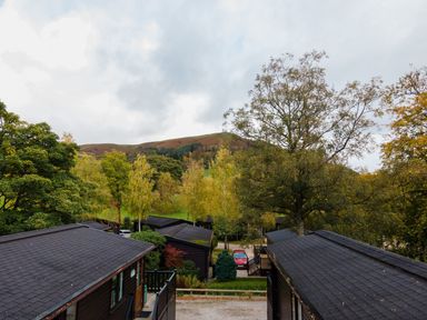 View over wooden lodges surrounded by trees with hills in the background at Rivendell Burnside Park Number 14 Burnside Park near Keswick