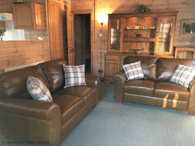A living room with two brown leather sofas and wooden cabinets at Rivendell Burnside Park Number 14 Burnside Park near Keswick