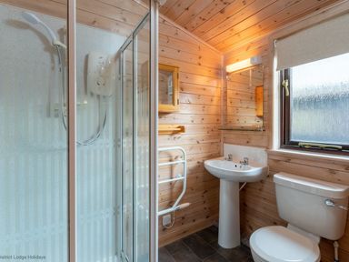 A bathroom with a shower enclosure a sink a toilet a window and wooden panel walls at Burr Ghyll Number 27 Burnside Park near Keswick