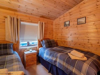 A bedroom with two single beds with plaid bedding a wooden drawer unit between them and wooden walls at Burr Ghyll Number 27 Burnside Park near Keswick