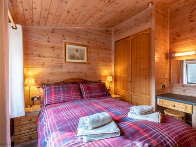 A bedroom with a double bed with plaid bedding two bedside tables with lamps a wooden wardrobe and a dressing table with a stool at Burr Ghyll Number 27 Burnside Park near Keswick