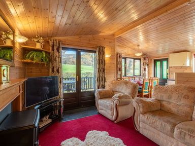 A living room with armchairs a television and dining table in a wooden cabin at Burr Ghyll Number 27 Burnside Park near Keswick