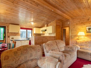 A living room with patterned sofas a kitchen area with white cabinets and a dining table with red tablecloth at Burr Ghyll Number 27 Burnside Park near Keswick