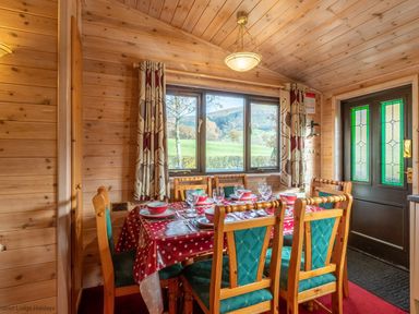 A dining room with a wooden table set with dishes and chairs near a window and door at Burr Ghyll Number 27 Burnside Park near Keswick