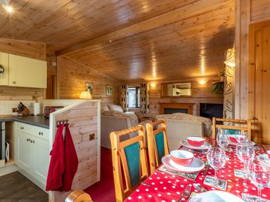 A dining table with red polka dot tablecloth set with bowls glasses and cutlery next to a kitchen and living room with wooden walls and ceiling at Burr Ghyll Number 27 Burnside Park near Keswick
