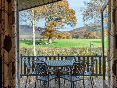 A patio with a metal table and six chairs overlooking green fields and trees at Burr Ghyll Number 27 Burnside Park near Keswick