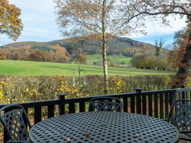 A metal patio table and chairs on a deck overlooking a field and hills at Burr Ghyll Number 27 Burnside Park near Keswick
