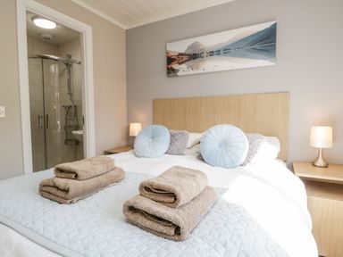 A bedroom with a double bed blue round cushions bedside tables lamps and an en suite bathroom at Troutbeck Lodge Beckside 6 Limefitt Park near Windermere