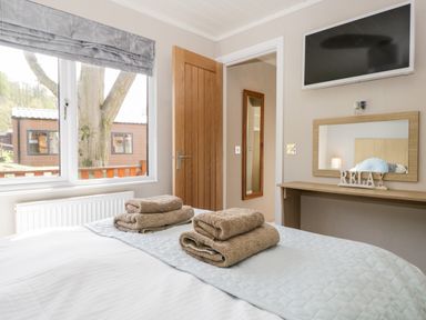 A bedroom with a bed with towels a window a wooden door a mirror a desk and a television at Troutbeck Lodge Beckside 6 Limefitt Park near Windermere