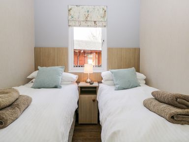 A bedroom with two single beds separated by a nightstand with a lamp and window at Troutbeck Lodge Beckside 6 Limefitt Park near Windermere