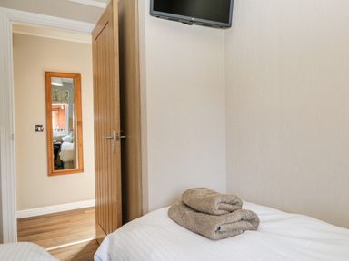 A bedroom with a wall-mounted TV towels on a bed and a door leading to a hallway with a mirror at Troutbeck Lodge Beckside 6 Limefitt Park near Windermere