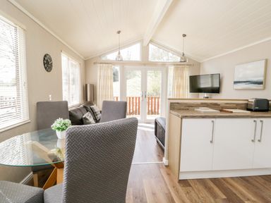 A dining area with glass table and chairs next to a living room with a sofa and TV at Troutbeck Lodge Beckside 6 Limefitt Park near Windermere