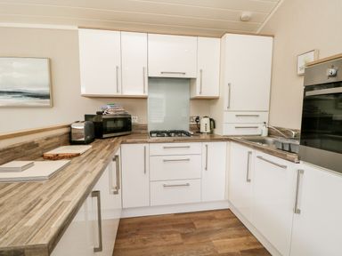 A kitchen with white cabinets wooden countertops a gas stove a microwave toaster kettle sink and oven at Troutbeck Lodge Beckside 6 Limefitt Park near Windermere