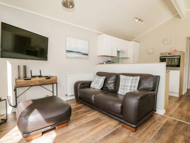A living room with a brown leather sofa and ottoman a wall-mounted tv and a wooden cabinet at Troutbeck Lodge Beckside 6 Limefitt Park near Windermere