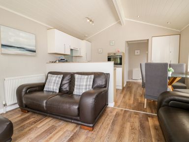 A living area with two brown leather sofas and kitchen cabinets along the back wall at Troutbeck Lodge Beckside 6 Limefitt Park near Windermere
