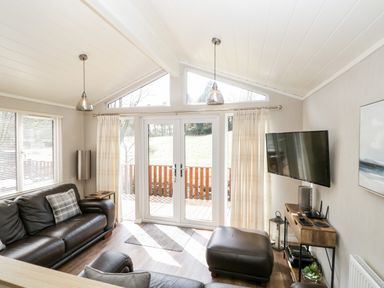 A living room with leather sofas a TV mounted on the wall and glass doors leading outside at Troutbeck Lodge Beckside 6 Limefitt Park near Windermere
