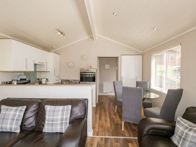 A kitchen and dining area with gray chairs around a glass table and a leather sofa with plaid pillows at Troutbeck Lodge Beckside 6 Limefitt Park near Windermere
