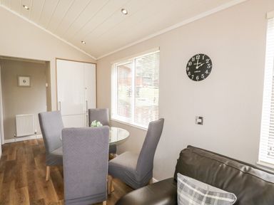 A dining area with four chairs around a glass table next to a brown leather sofa and a black wall clock at Troutbeck Lodge Beckside 6 Limefitt Park near Windermere